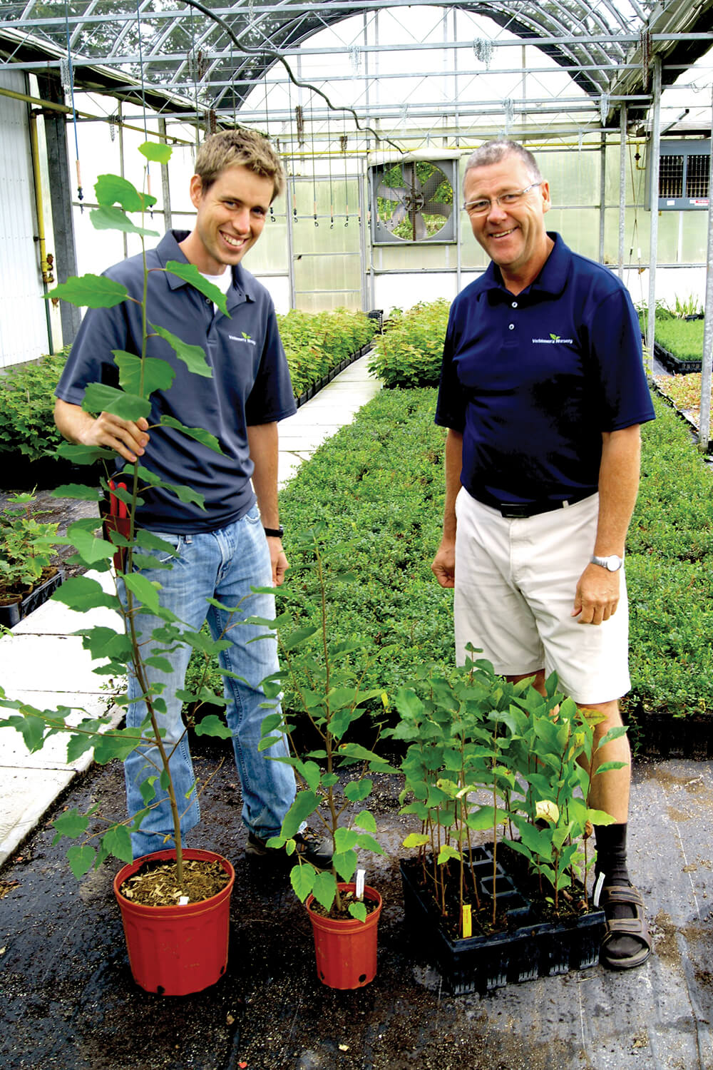 two men in a greenhouse showing off plants