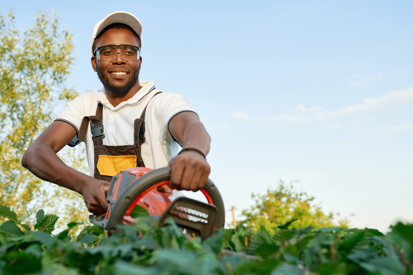 A young person using a hedge trimmer with a blue sky background