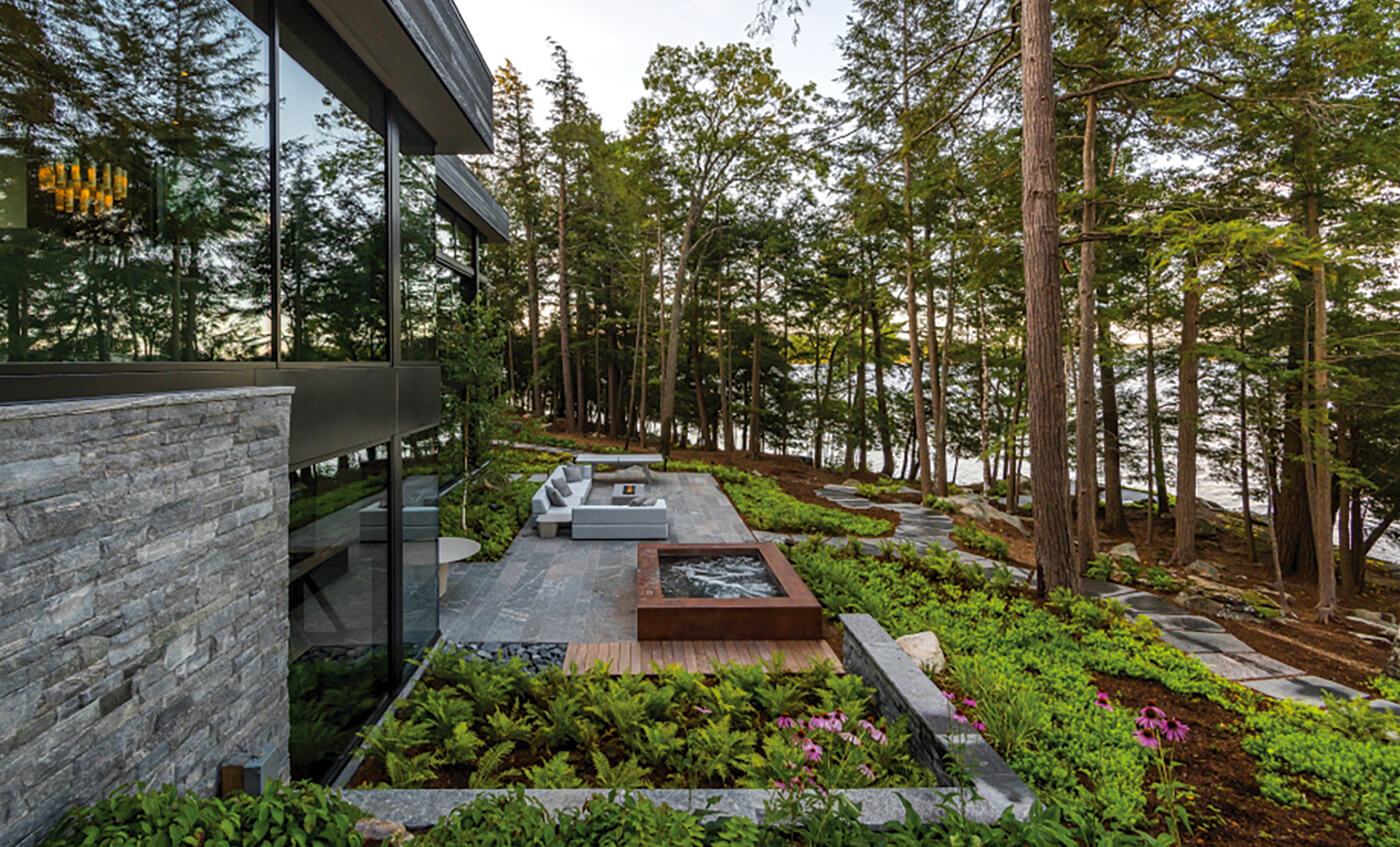 A patio behind a house overlooking a wooded slope down to a lake