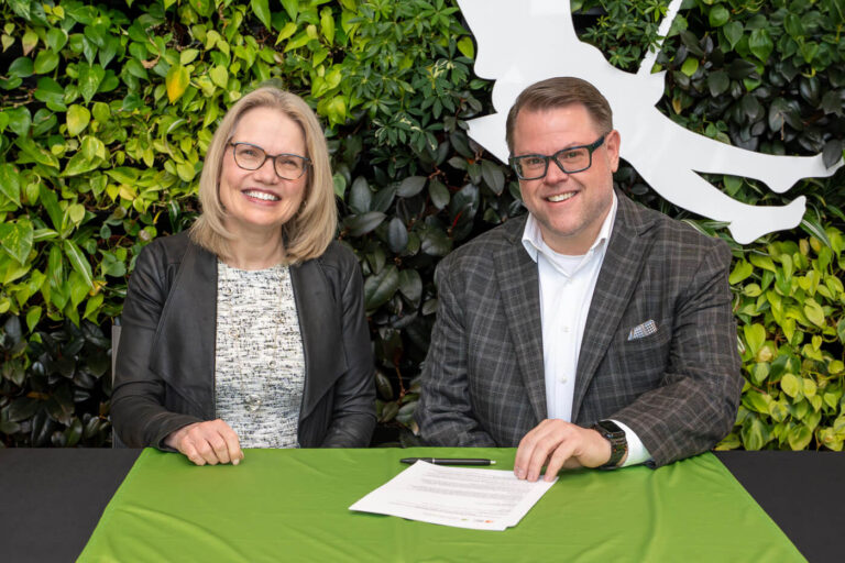 A woman and a man seated at a table with a green tablecloth and living plant wall in the background