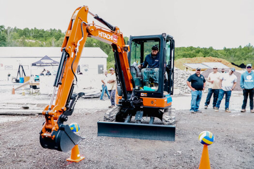 A person using an excavator to place a volleyball on a pylon