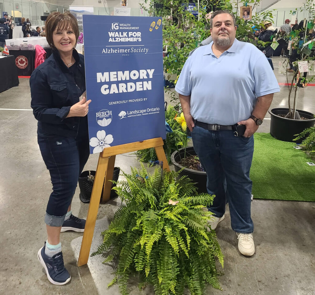 A woman and man standing beside a sign in an indoor garden