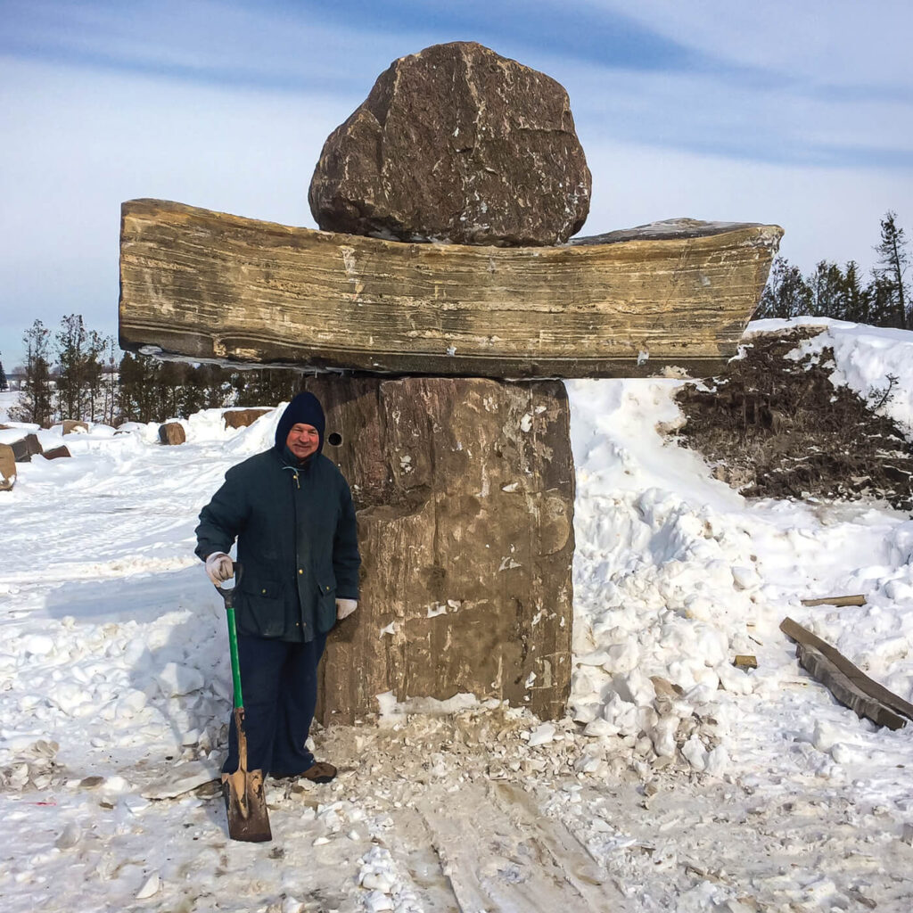 A man standing at the base of a large stone statue about twice his height in winter