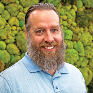 Headshot of a man with a long beard wearing a pale blue shirt